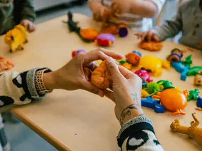 Photo of hands playing with playdough surrounded by small plastic dinosaur toys.