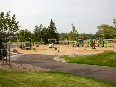 Playground with slides and swings next to a paved trail and trees nearby