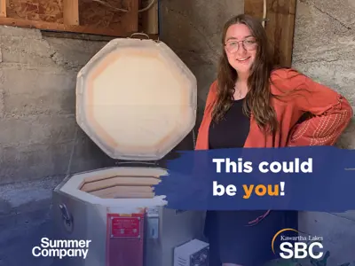 Young woman in an orange cardigan standing in front of a pottery kiln. A text overlay reads, 'This could be you!'