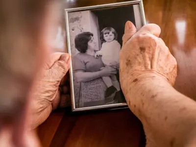 Photo of elderly hands holding a black and white photograph of a woman and a young chiled.