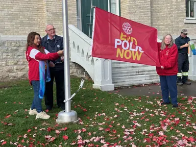 Red flag with text reading 'End Polio Now' being raised in front of old brick building.