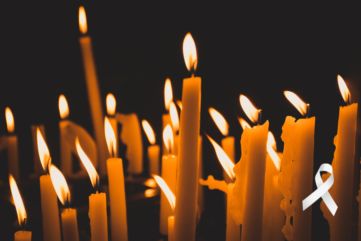 Photo of candles burning in the dark. The background is pitch black, and there is a white ribbon graphic in the lower right corner.