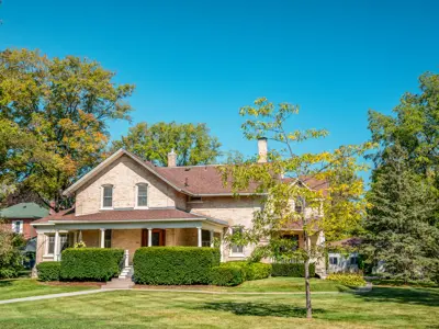Light brick house surrounded by a few trees and a blue sky