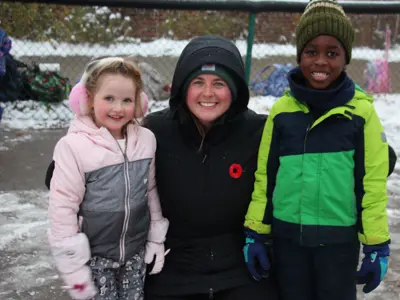 Photo of two children on either side of an adult. All three are outdoors and wearing cold weather clothing.