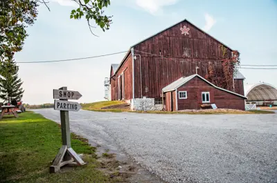 Red barn with a gravel laneway and two arrow signs that read Shop and Parking.