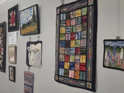Photo of a variety of hooked rugs hung on a grey wall.